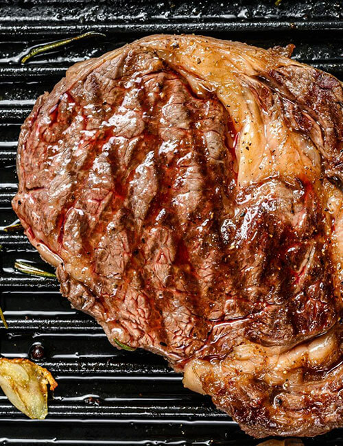 grilled-rib-eye-ribeye-steak-in-a-pan-gray-background-top-view.jpg
